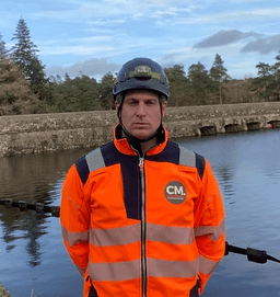 John Donaldson, Director of Corrosion Management Ltd, in orange safety equipment by water infrastructure demonstrating 17+ years of corrosion protection expertise